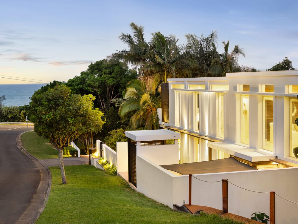 Angkasa's illuminated white coastal residence, palms and ocean at twilight
